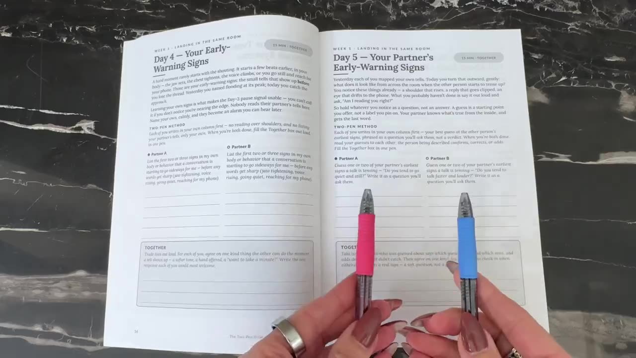 The workbook held up beside two pens